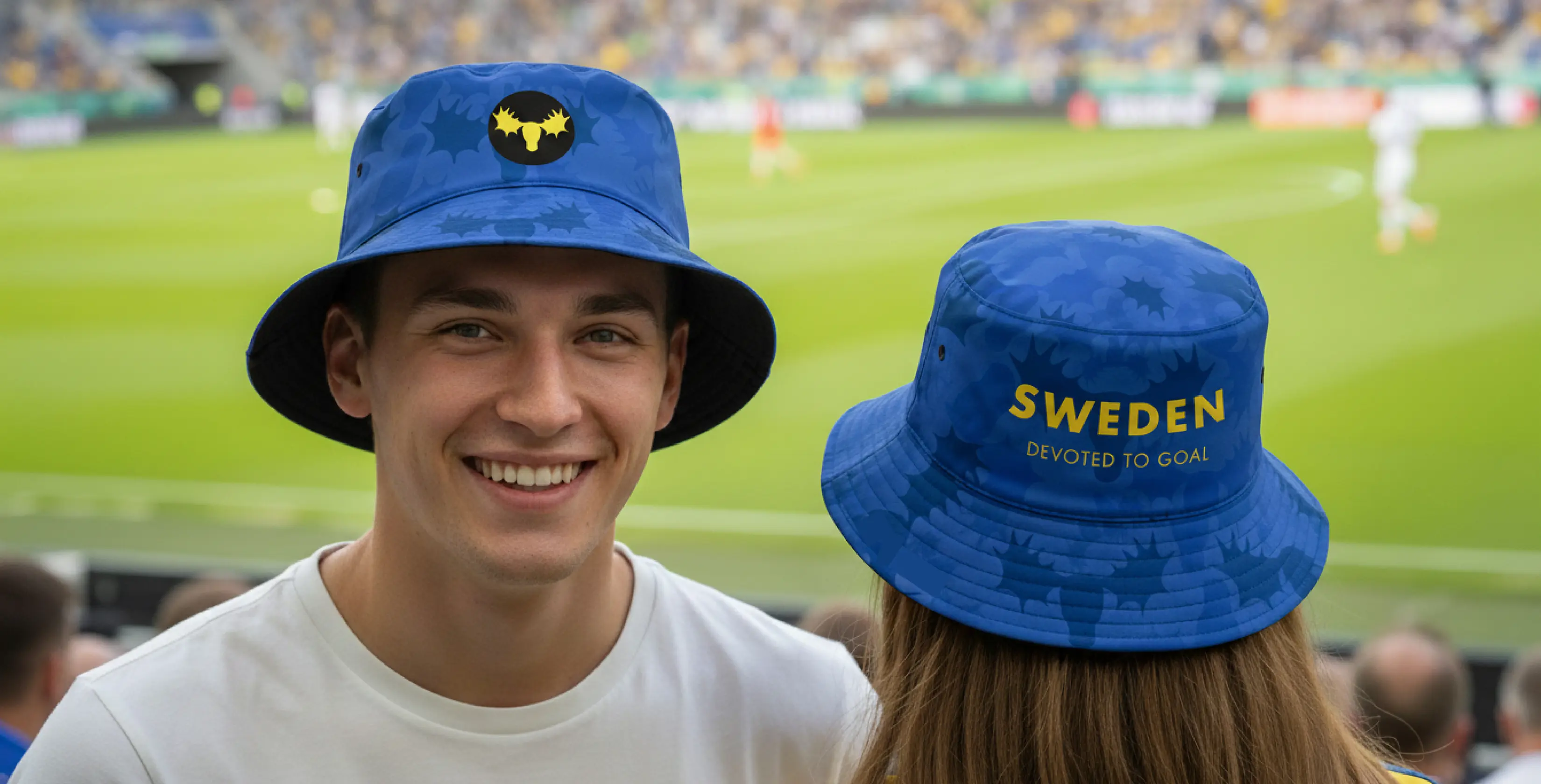 Tv&aring; personer i bl&aring; "Sweden Devoted to Goal"-bucket hats p&aring; en arena.